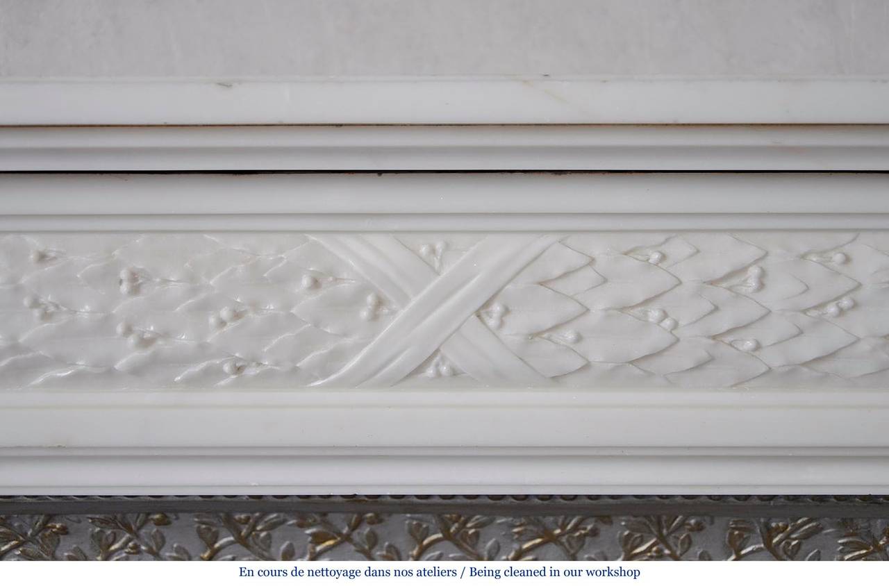 This antique Louis XVI style fireplace was carved in Statuary Carrara marble during the 19th century. The frieze is fully carved with laurel leaves. Both legs are fluted. 
The fireplace is sold with its original cast iron insert but without any