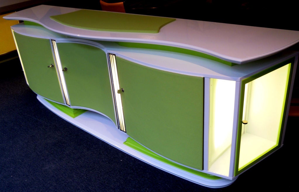 A very nice combination of art-deco and modern art.
White and green lacquered art-deco sideboard.The doors and the top is recovered with a matching green leather.In the front and on both sides with lighting inside of the panels.