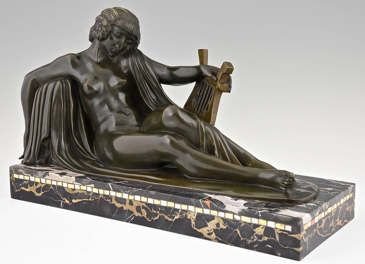 Reclining nude with lyre. 
By Marcel André Bouraine, 1886-1948. 
Signature:  A. Bouraine.
Style:  Art Deco. 
Date: circa 1925-1930.

Material: Bronze, green patina.  Portor marble base with glass inlay. 
Origin:  France. 
Size:  
L. 19.3
