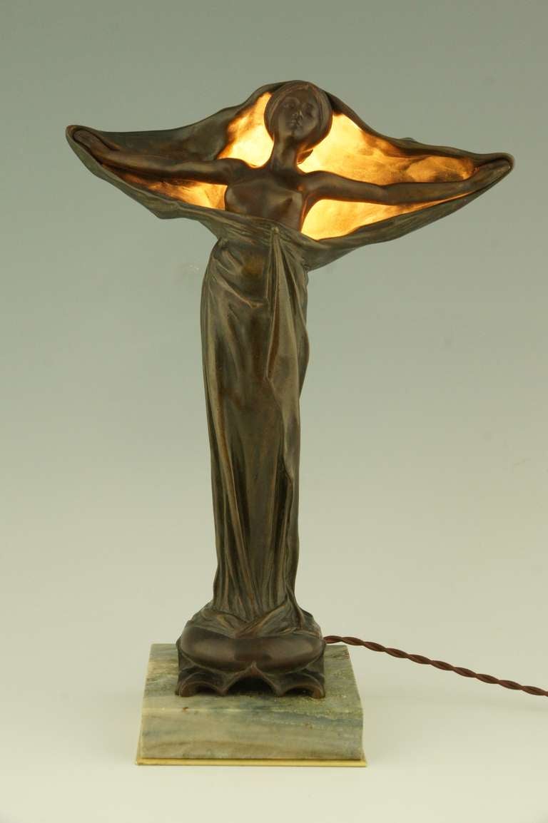 An Art Nouveau bronze lamp depicting a woman with outstretched arms removing her scarf to reveal her face and bare breasts. 
Signed by  Victorin Sabatier. 
 Louchet foundry mark. 

Literature: 
“Etains 1900” Philippe Dahan, les éditions de