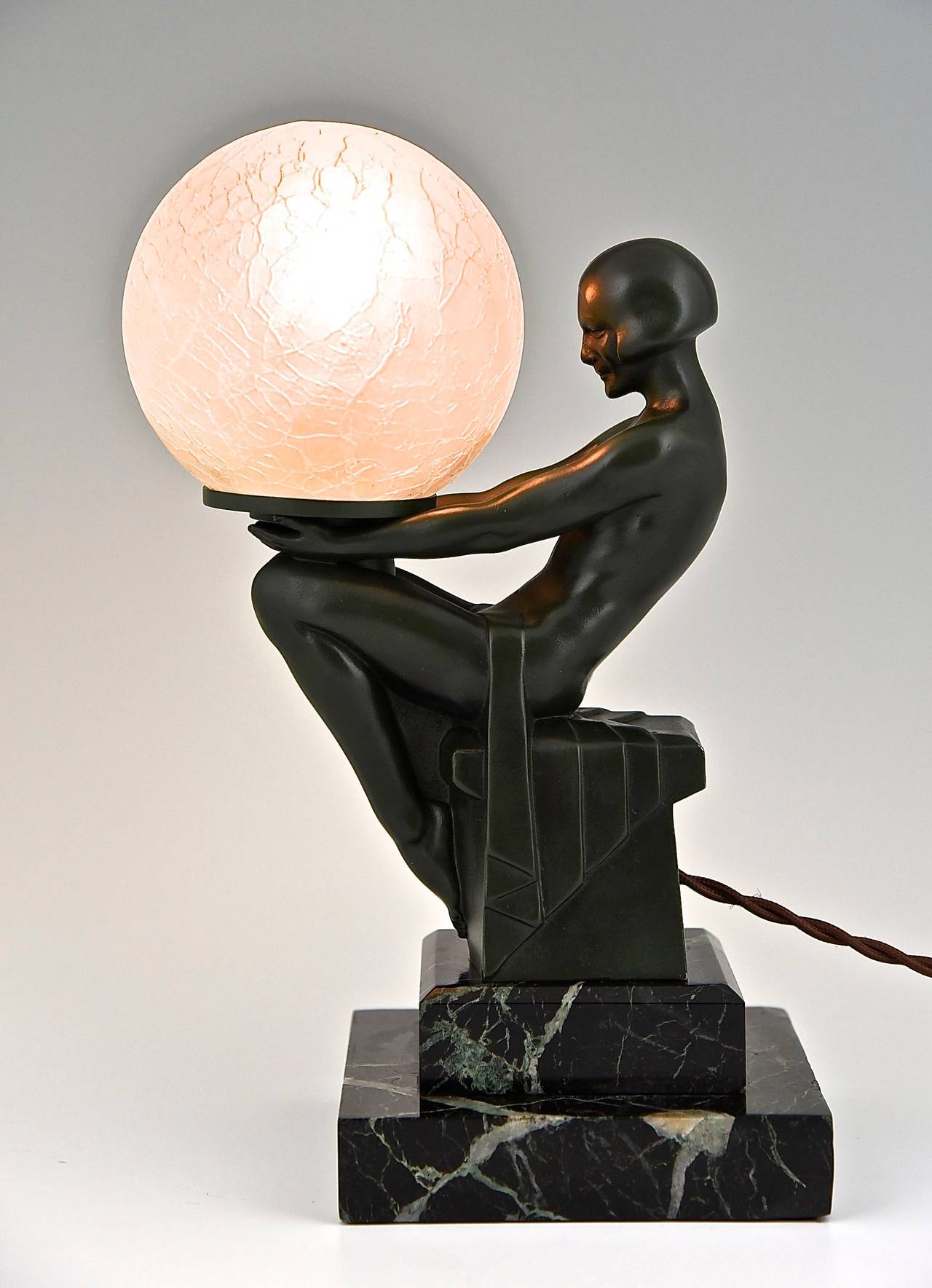 Art Deco figural table lamp of a sitting nude holding a glass shade.
Artist / Maker: Max Le Verrier. 
Signature / Marks: M. Le Verrier. 
Style:  Art Deco. 
Date: 1930.
Material: Dark green patinated metal.  Marble base.  Crackled glass shade.