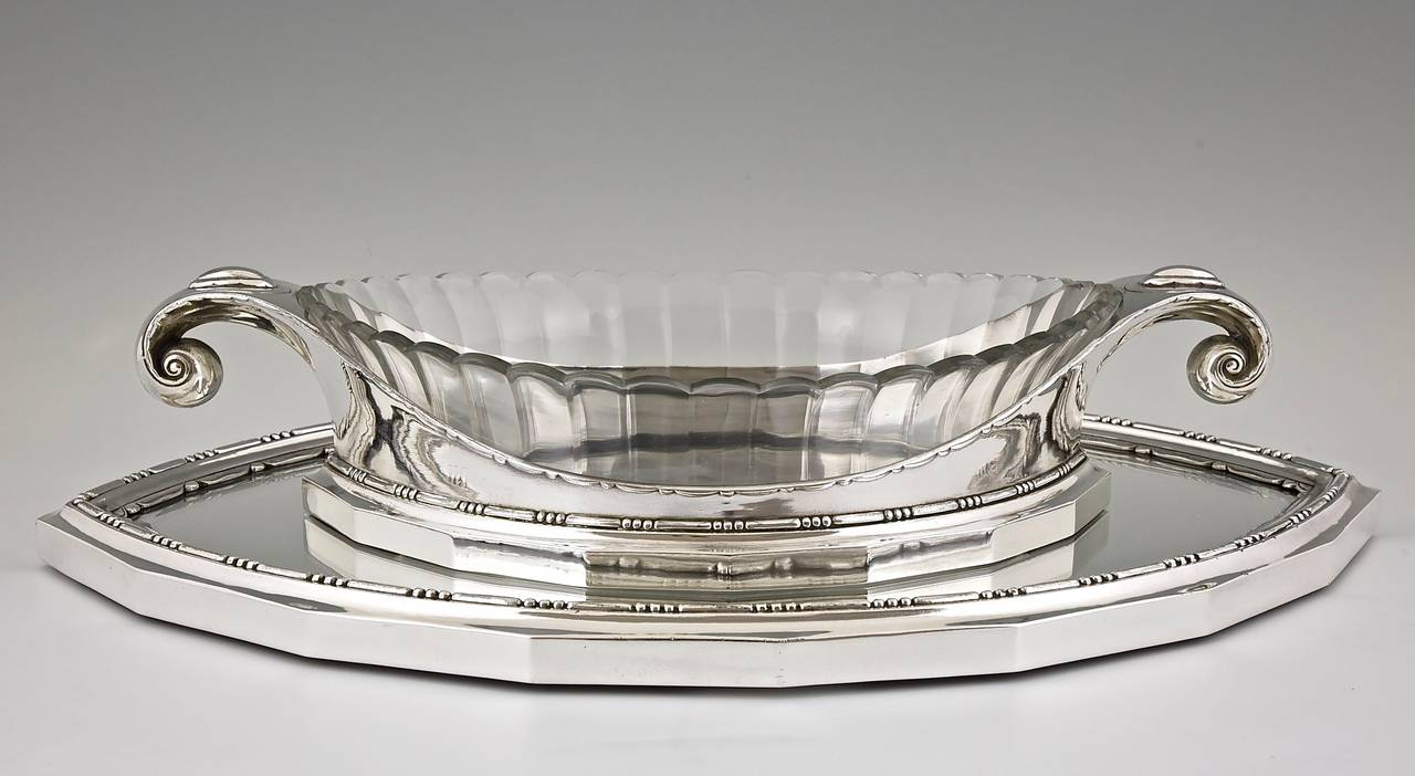 An Art Deco silver plated centerpiece with a cut glass liner and a mirror plateau with bevelled glass. 
Artist/ Maker:  Gallia, Christofle.  Design by Sue et Mare for Gallia. 
Signature/ Marks: Gallia stamp, numbered 5865 & 5830.   
Style: 