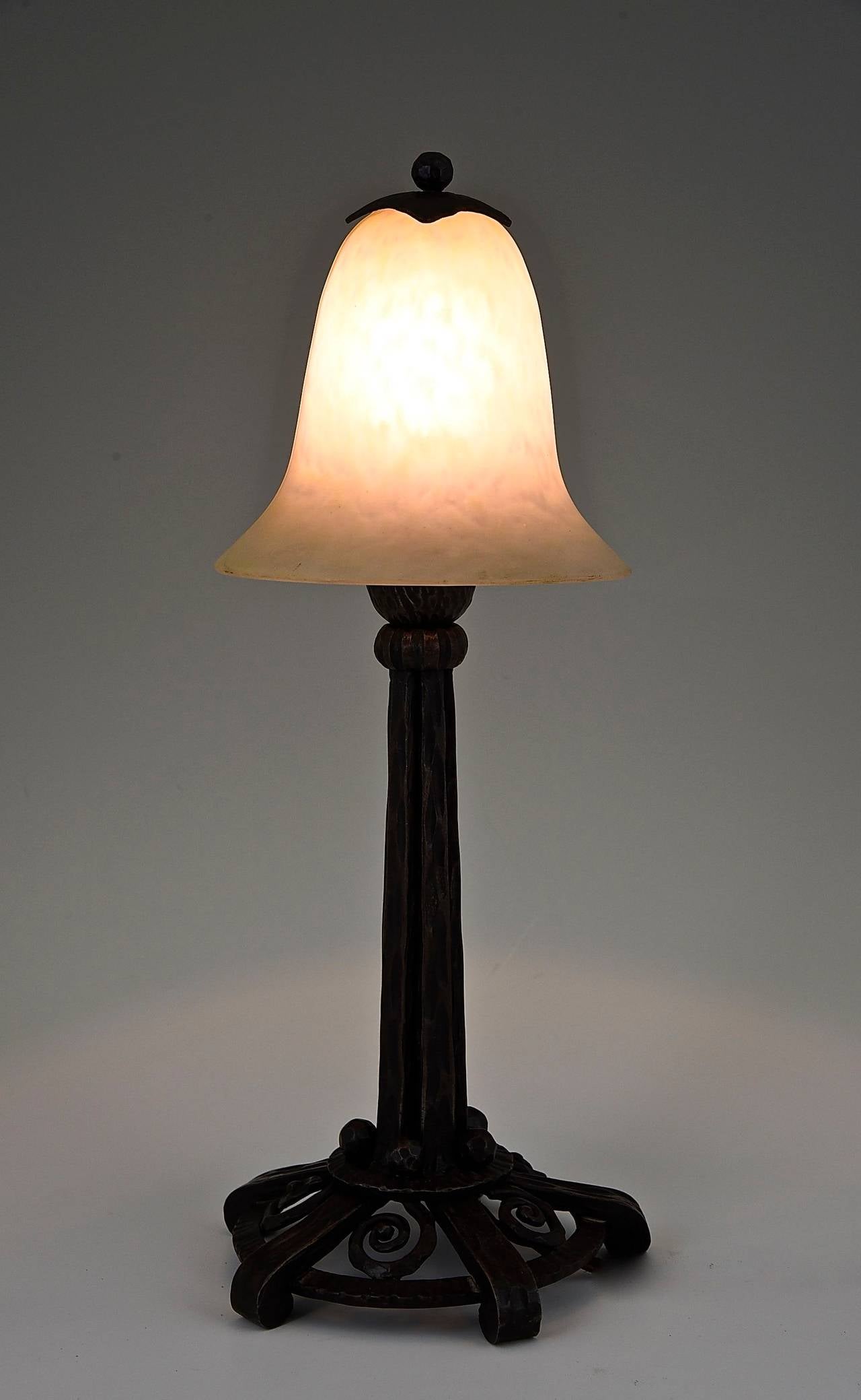 A Schneider table lamp.
Artist/ Maker:  Charles Schneider. 
Signature/ Marks:  Schneider on the glass shade. 	 
Style:  Art deco. 		
Date:  1924-1928.			
Material:  Cloudy off white and yellow glass shade on a fine wrought iron base. 
Origin: