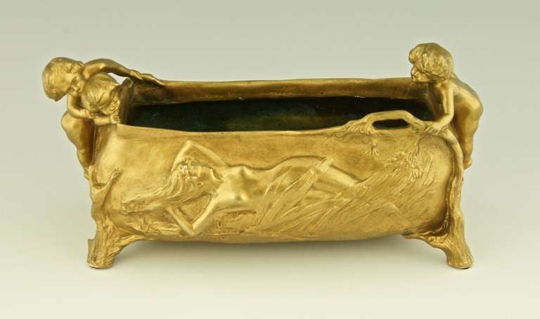 A gilt bronze jardiniere decorated with a nude lying in a field.Three little boys are peeping over the rim. By Charles Korschann, Paris. 

This model is illustrated on page 1003 of 
“Bronzes, sculptors and founders” by H. Berman,