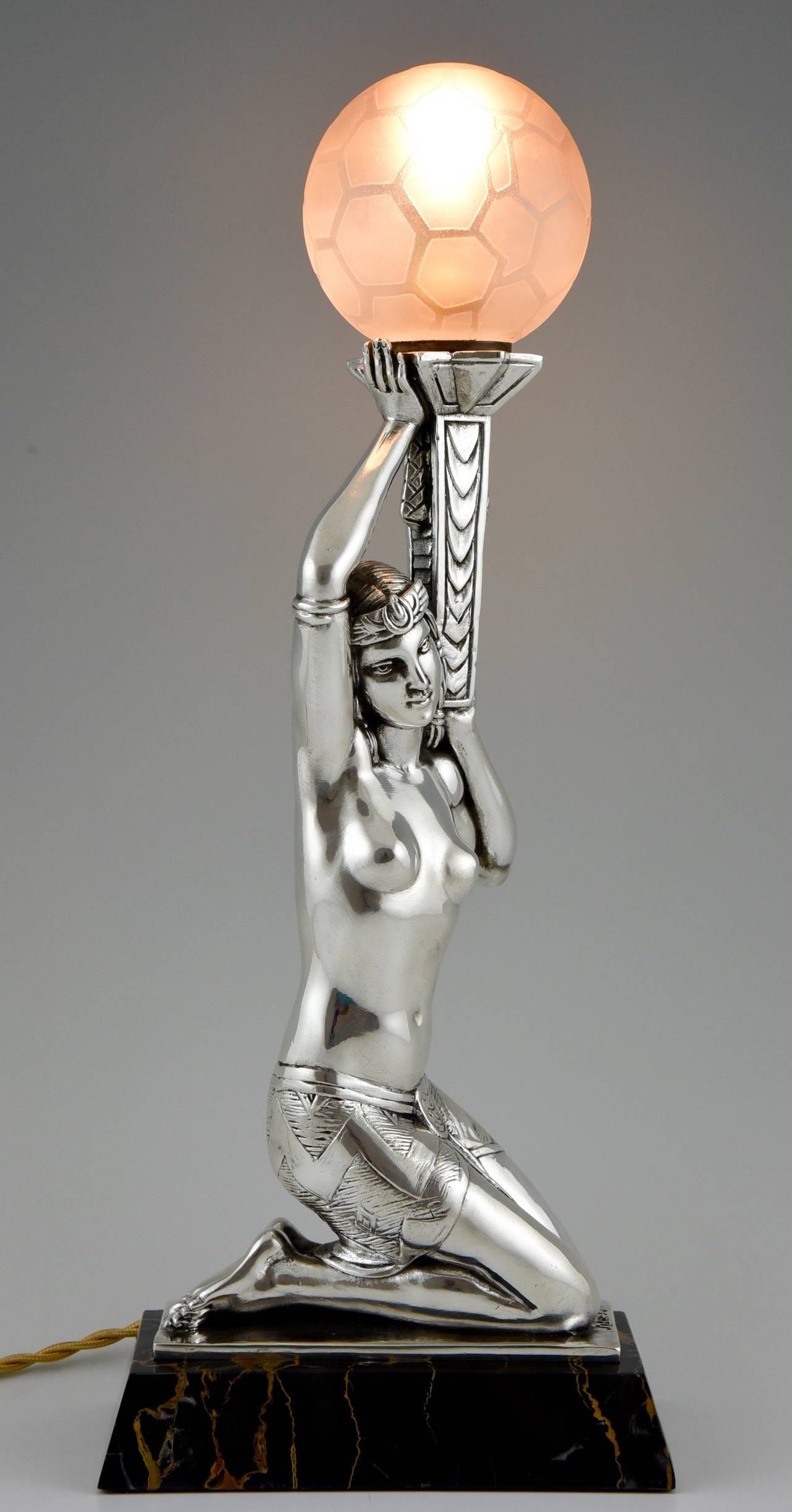 Art Deco figural table lamp of a seated nude holding a glass shade.
Signed by Salvado.
Date:  1930.
Material: Silvered metal. Portor marble base.  Glass shade. 
Origin:  France. 
Size:  
 H 16.1 inch x L 6.5 inch x W 3.3 inch.
H 41 cm. x L