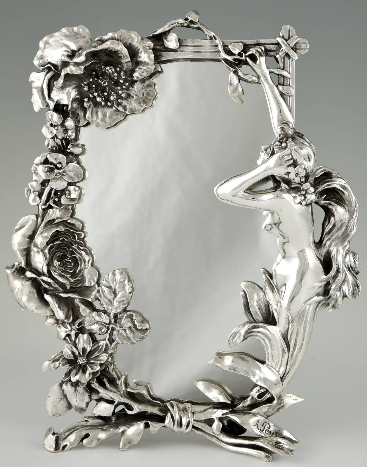 Description:  Art Nouveau silvered table mirror with a lady picking flowers to put in her hair. The frame decorated with flowers. 
Artist/ Maker:  Peyre, Raphael- Charles.  France, 1872-1949.
Signature/ Marks:  Peyre.
Style:  Art Nouveau.