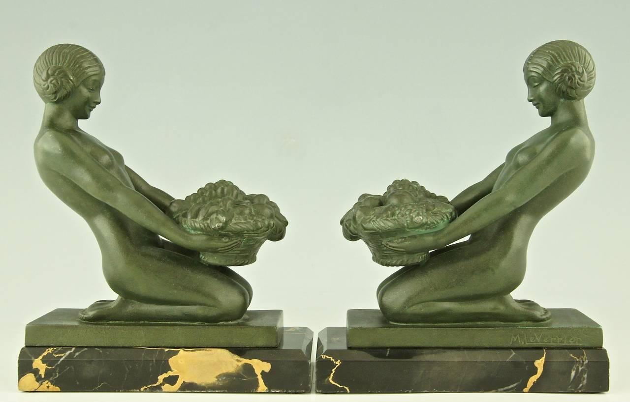A pair of Art Deco bookends with kneeling nudes holding baskets full of fruit. 
by Max Le Verrier. 
Signature: M. Le Verrier. 
Style:  Art Deco. 
Date:  1930.
Material: Dark green patinated metal.  Portor marble base. 
Origin:  France.