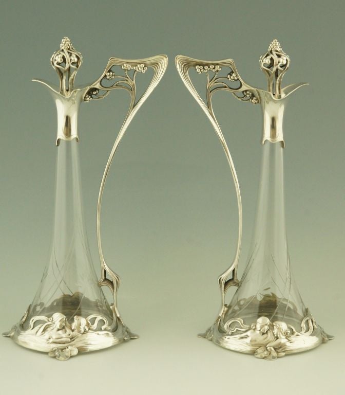 Fedex shipping: $ 265.

A pair of Art Nouveau claret jugs decorated with ladies and flowers with finely cut glass.

WMF, Württembergische Metallwaren Fabrik. 
WMF mark 0/1, B.

Picture on page 37 and Illustration number 191 of the book
”Art