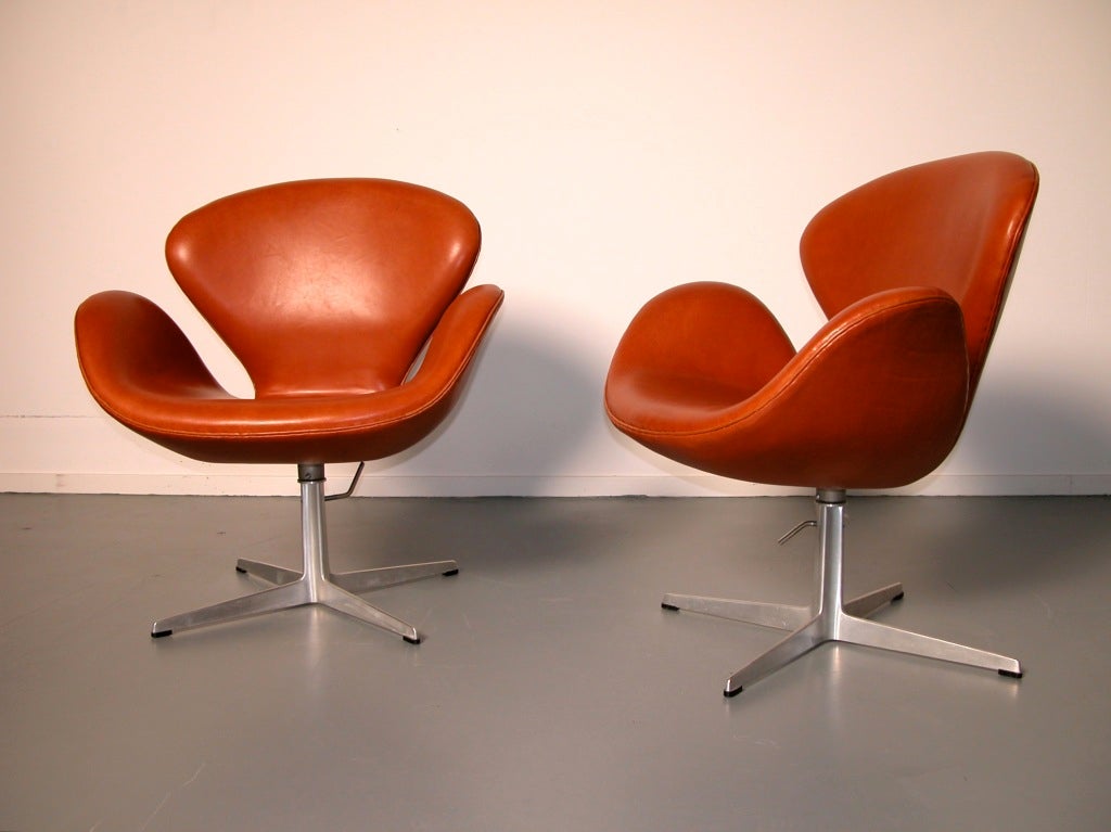 Matching pair of Swan Chairs in cognac colored leather. 
The chairs have the very rare option of height adjustability, so you could use them as a desk or dining chair as well.
The chairs have recently been reupholstered by the finest Danish