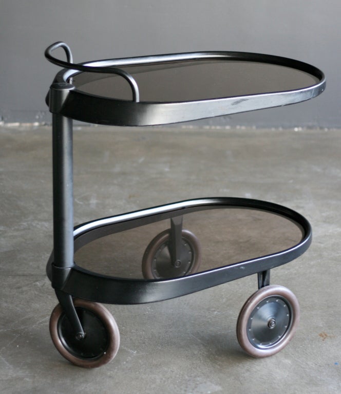Tea trolley designed by Enzo Mari for Alessi.
Handlebar above a cylindrical shaft side support, on three wheels, stamped Alessi.