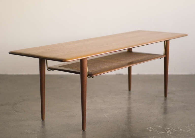 Coffee table by Danish design firm Hvidt & Mølgaard early 1960's. The rich solid teak top and the teak framed/caned shelf below, are connected with small brass pins.