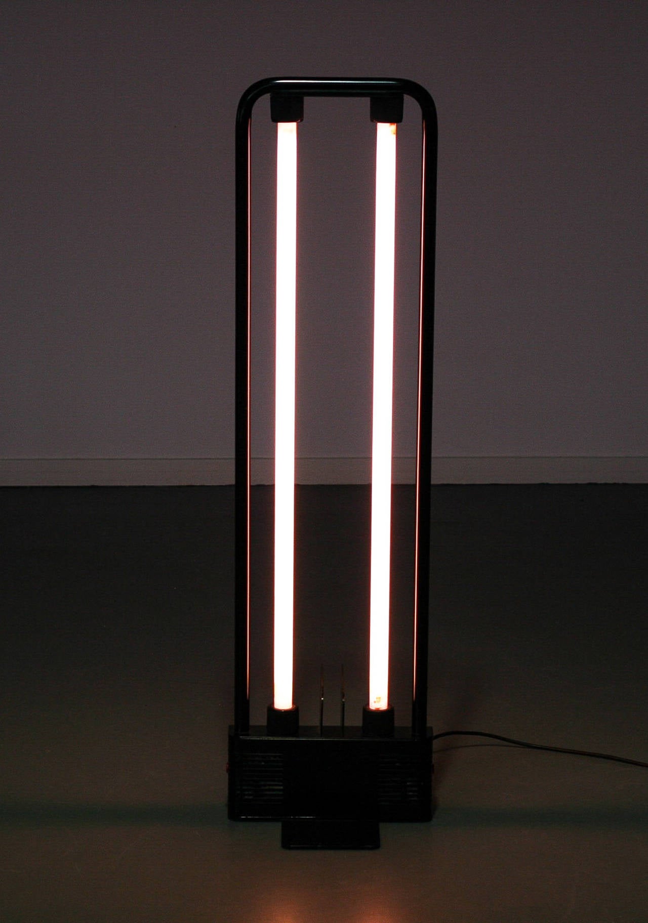 Modern floor lamp, designed by Gian Nicola Gigante for Zerbetto Italy in 1981. Simple floor lamp that can also be used as an object. Black metal base and frame with two fluorescent tubes of 36 W.
The pink selves on the tubes can be removed for a