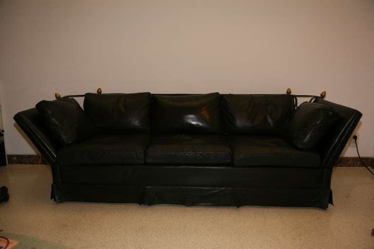 a three place sofa in black leather with armrests attached to backrests by leather straps and large buckles in gilded bronze.
Circa 1960.