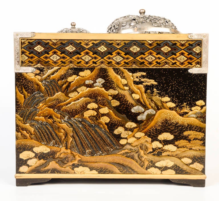 Japanese lacquer Tabakobon decorated with waterfalls in a mountainous landscape with trees. Three drawers, two metal containers with engraved silver metal flowering cherry branches and openwork caps.

Provenance: Private Collection descendants of