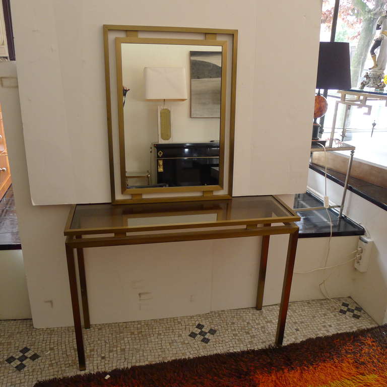 A console table in bronze with a glas tabletop and a mirror in bronze.