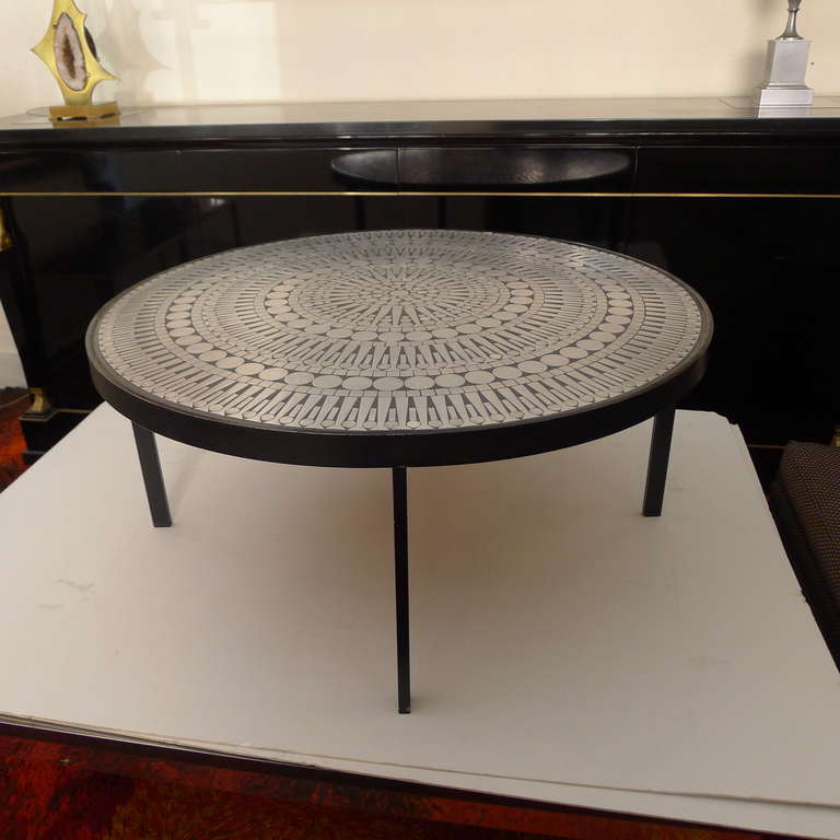 A cocktail table featuring a simple frame in black lacquered steel with a top composed of deep grey resin inlayed with pieces of polished steel creating a multi-circular modernist pattern.