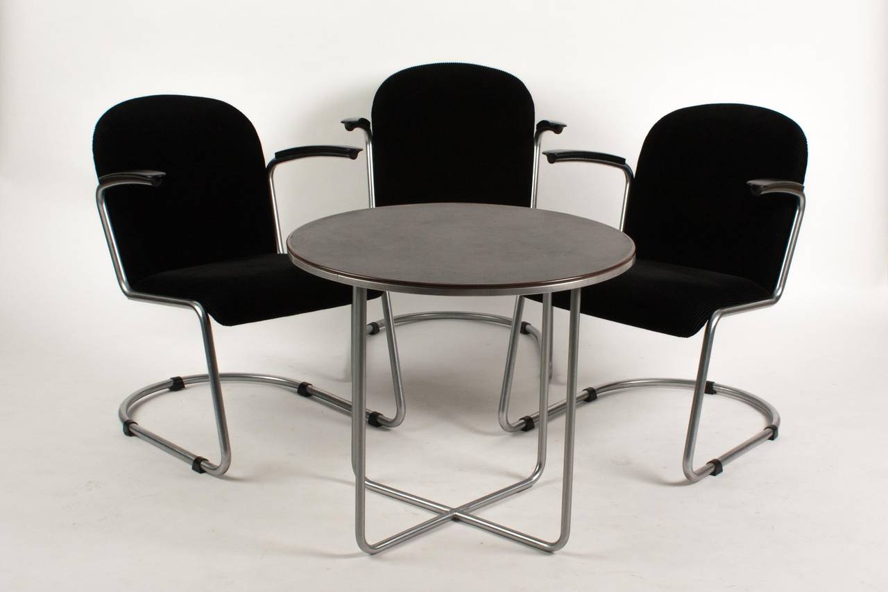 A table and three chairs of Dutch designer Willem Gispen. The chairs are for lazy sitting and the table is of metal with a black Marmoleum top. The edge is of brown bakelite. Diameter 70 cm and 61 cm is the height. The chair are with Gispen black