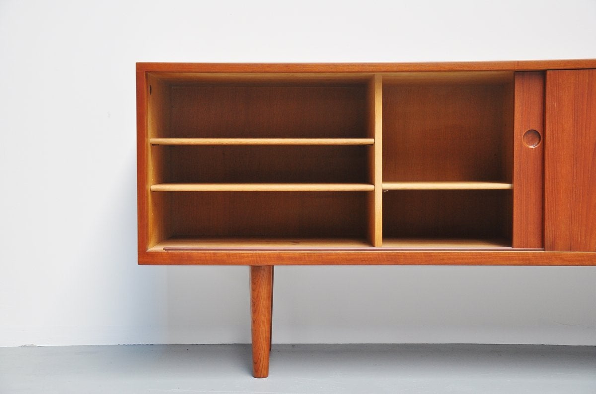 Very nice teak sideboard designed by Hans J. Wegner for Ry Mobler, Denmark, 1965. This nicely crafted simple sideboard has two sliding doors with five shelves and four drawers behind. This sideboard has very nice round integrated handles and a very
