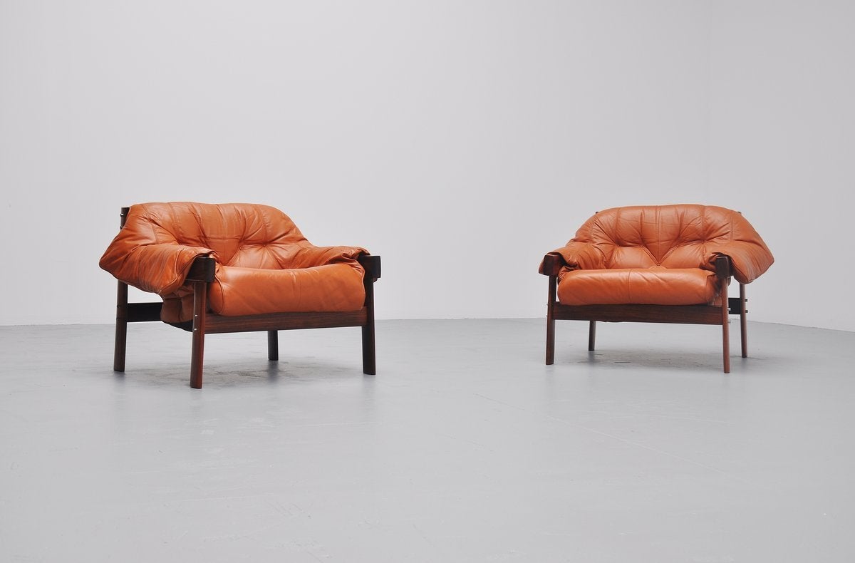 Spectacular pair of lounge chairs designed by Percival Lafer for Lafer MP, Brazil, 1961. These lounge chairs have a solid rosewood frame and the cognac leather cushions rest on natural leather straps mounted with wooden knobs. Super nice set of two