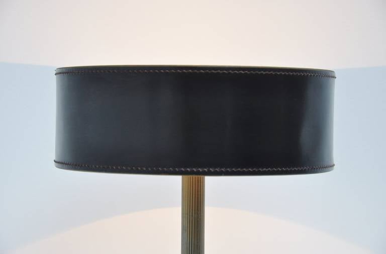 Leather-clad table lamp with hand stitched shade and square base. Comprised with a reeded polished brass stem.