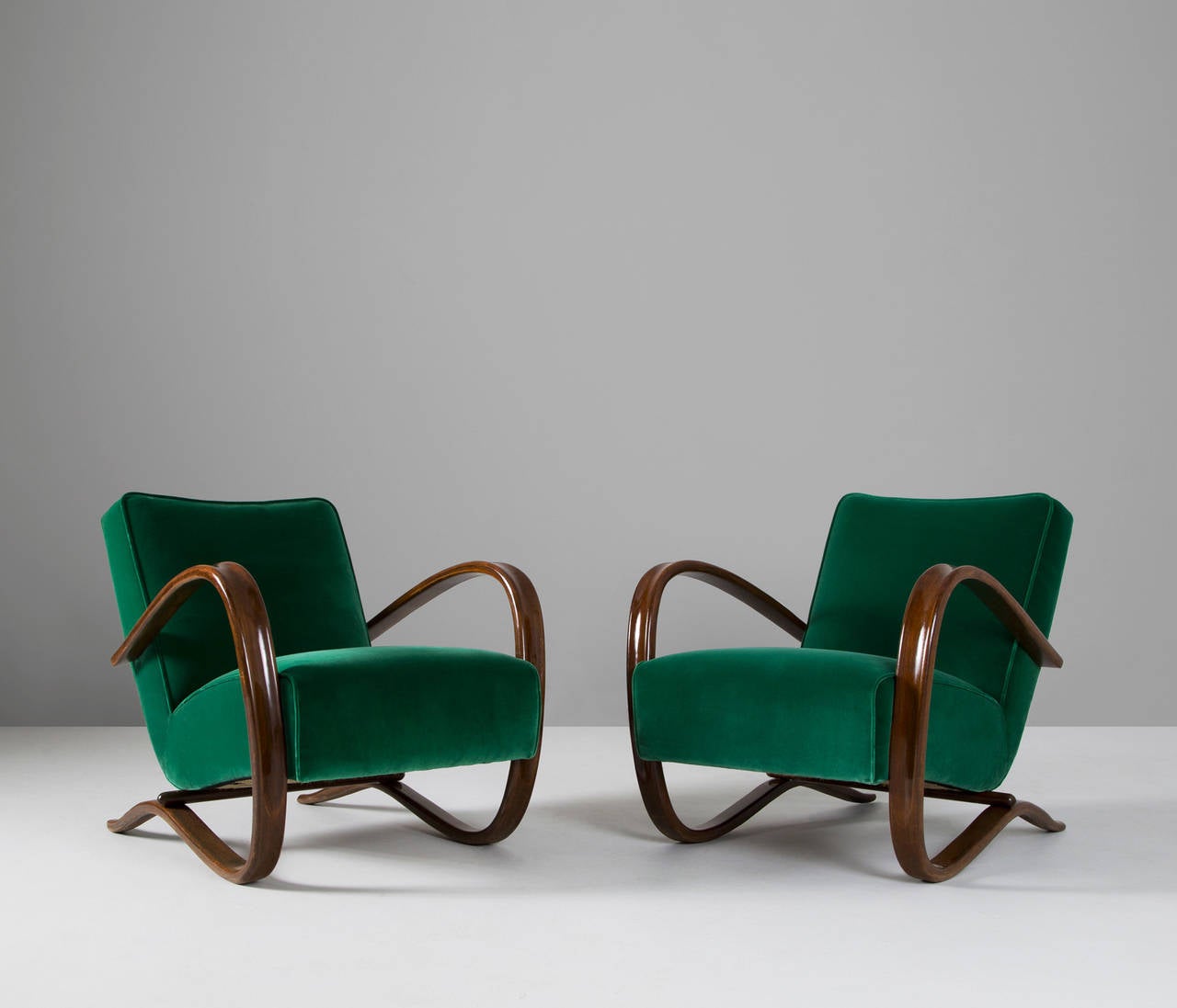 Pair of lounge chairs, in wood and green fabric, by Jindrich Halabala, Czech Republic, 1930s. 

Very dynamic chairs with a curved base that fluently ends in the armrests.
These chairs are completely refurbished and reupholstered in a green velvet