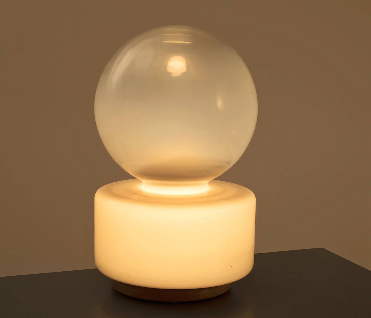 Opaline glass table lamp with pine wooden base. 

Very basic shape, with friendly proportions and soft edges. The opaline white spherical top is illuminated indirectly by the dark grey opaline glass cylindrical bottom element.
The lamp was very well