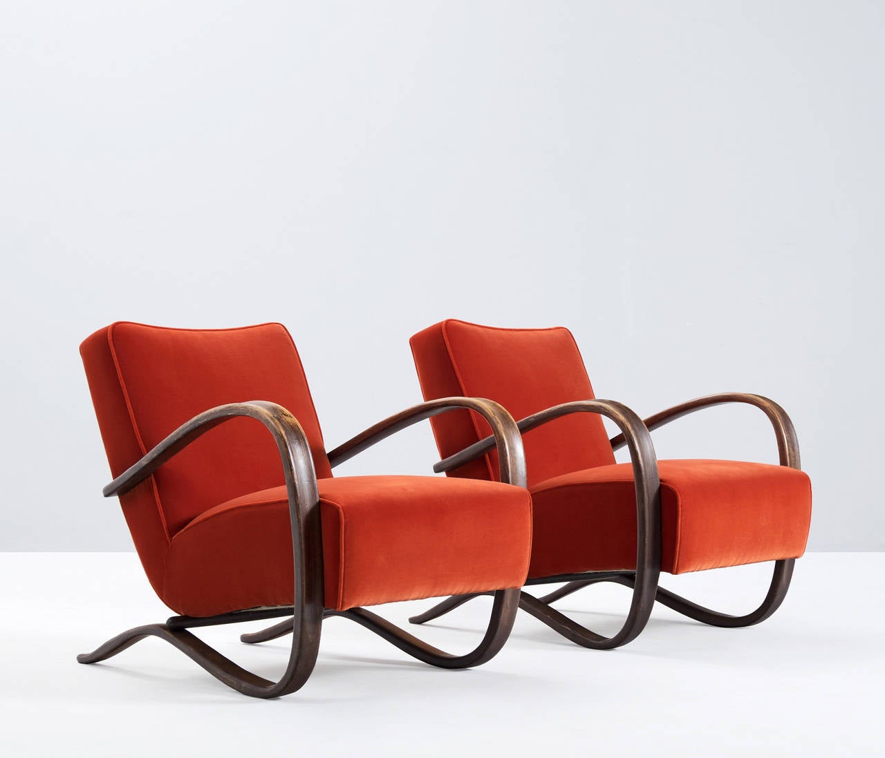 Jindrich Halabala, armchairs, beech and fabric, by Czech Republic, 1930s. 

These chairs have a very dynamic appearance, due the curved base that ends fluently in the armrests. The dark brown stained wood nicely combines to the red velvet like