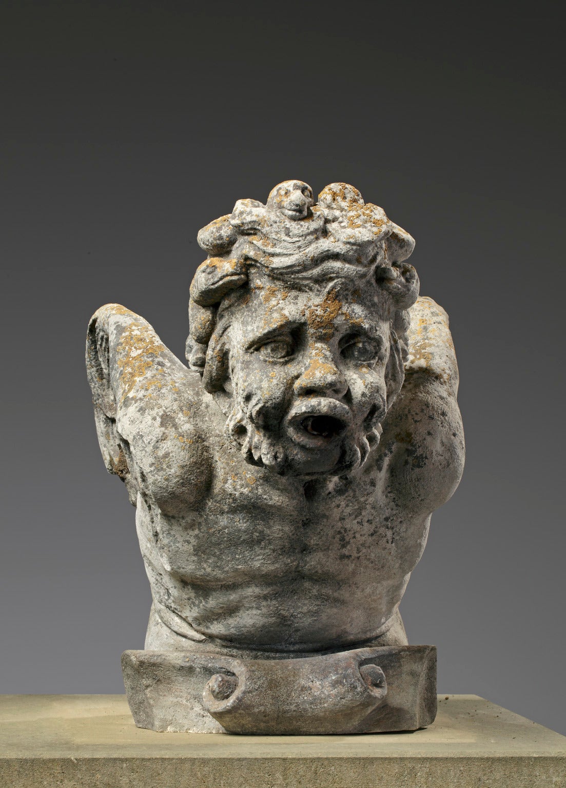 This gargoyle/fountainhead was made in France in the 19th century. It is sculpted in the shape of a bearded man. His facial features remind of Bacchus, the Roman god of wine. His mouth is opened wide, so water can flow from his mouth.

His arms