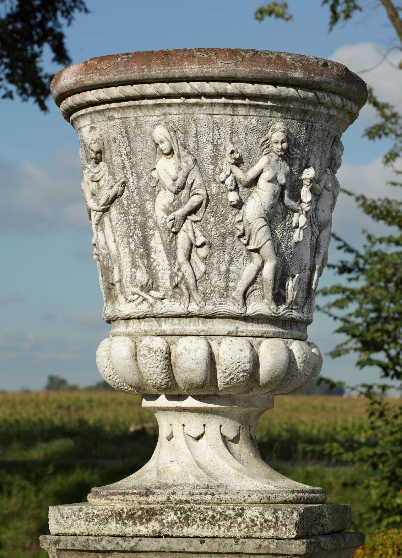 Large Continental reconstituted stone garden urn of circular section and tapering form, the knopped rim above a frieze of dancing maidens, with waisted socle and square section base.
