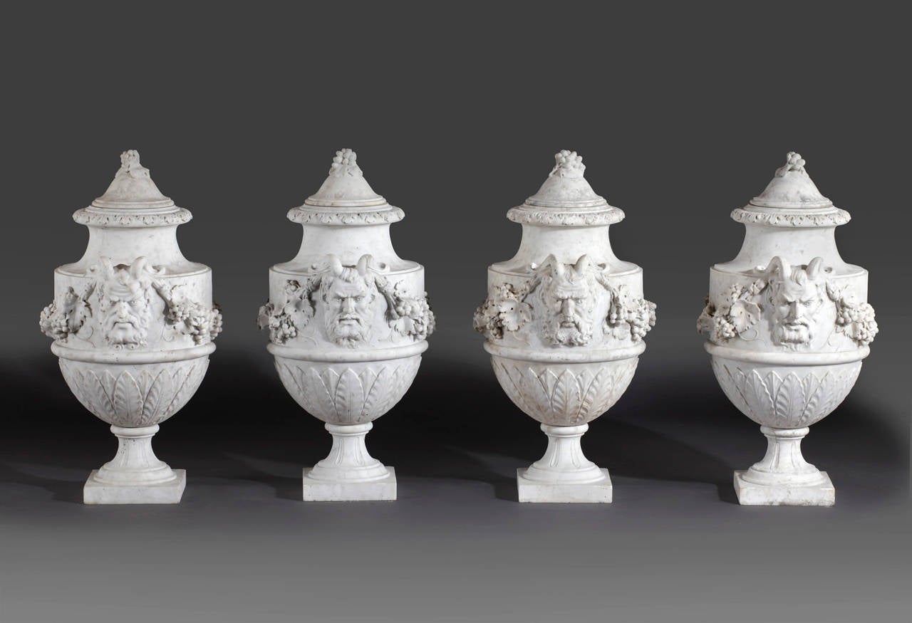 A set of French sculpted white marble vases in neoclassical style, late 19th century, each with domed top to a slender neck, above twin Bacchic masks united by foliate swags to each side, above leaf clasped undersides, waisted socles and square