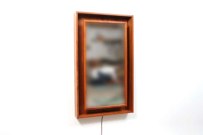 Backlit teak mirror by Pedersen & Hansen.  This rectangular mirror features a shadowbox teak frame with a floating mirror that lights up from behind.  Provides a pleasing ambient light.  Mirror and lamp in one.