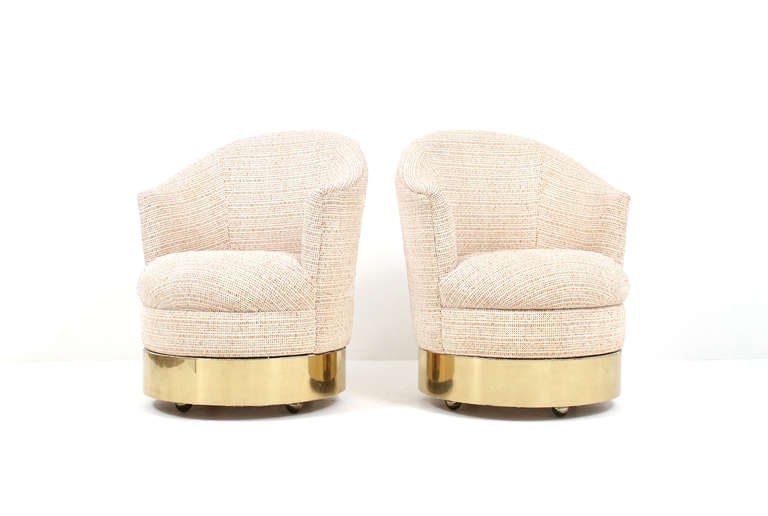Attractive pair of Karl Springer upholstered swivel lounge chairs.  These chairs are supported on a wood base with brass trim and sit on 4 castors.  Comfortable and mobile seating.