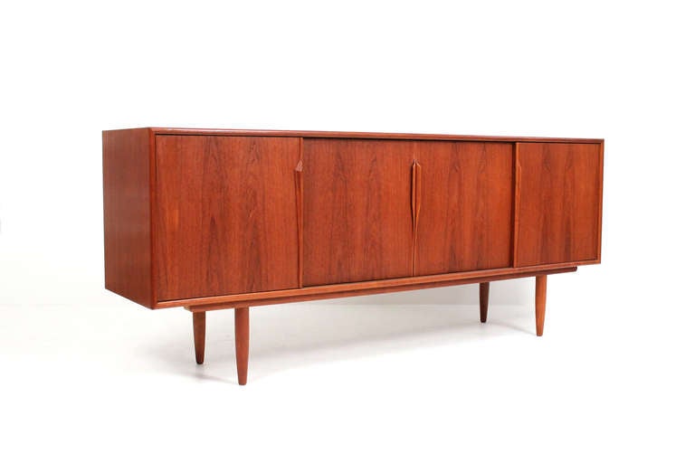 Attractive teak credenza sideboard designed by Gunni Omann for Axsel Kristiansen.  It features four sliding doors with sculptural handles and an interior of drawers and shelves to accommodate varying storage needs.