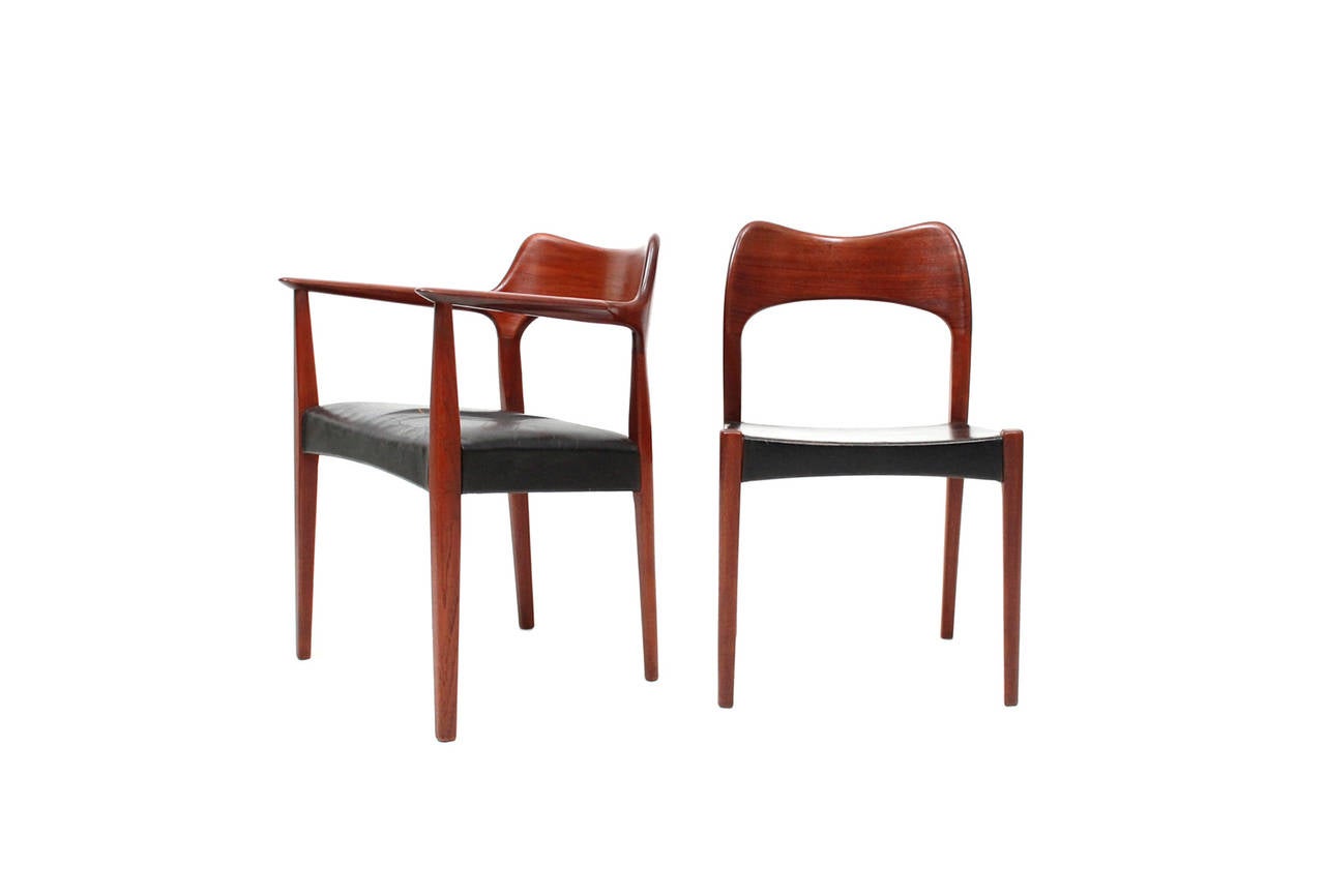 Set of 8 teak and leather dining chairs designed by Arne Hovmand Olsen for Danish cabinetmaker Mogens Kold.  Chairs feature teak frames and back support with black leather seats.  Useful set of dining chairs with subtle sculptural design qualities. 