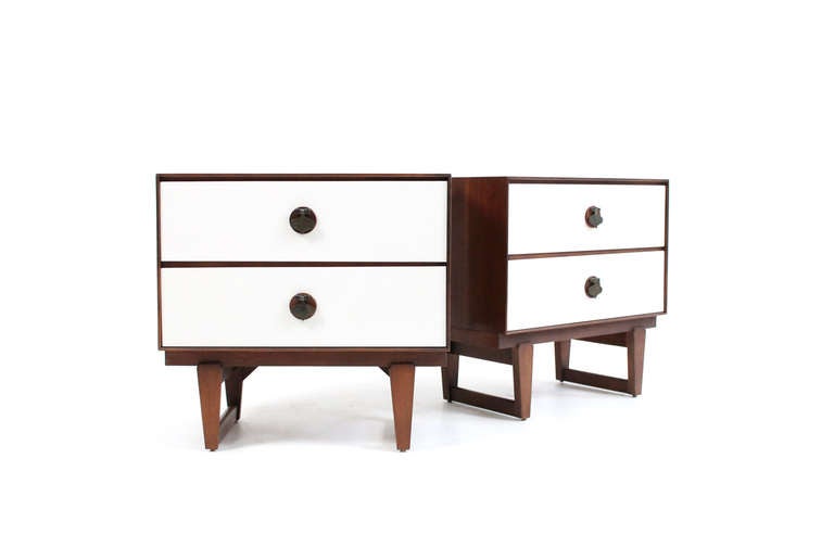 Pair of walnut and white lacquer nightstands by Stanley. These nightstands feature sled legs and solid brass pulls in the shape of spades that hang over walnut medallions. Fun and attractive pair of nightstands.