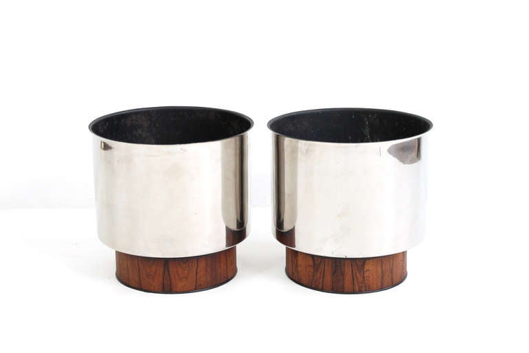 Large scale stainless steel planters with rosewood bases.  1960s.  Suitable for large plants or small trees.  Steel planters rest on circular rosewood plinths.  Very useful pair of planters for home or office.