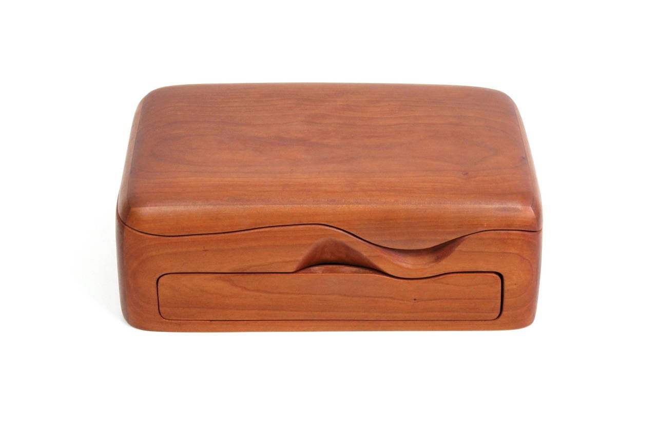 Sculptural studio craft jewelry box in cherry. Box has one drawer and its top lifts revealing another large compartment, circa 1970s and signed to the reverse with the artist's mark. Interior lined in period fabric.