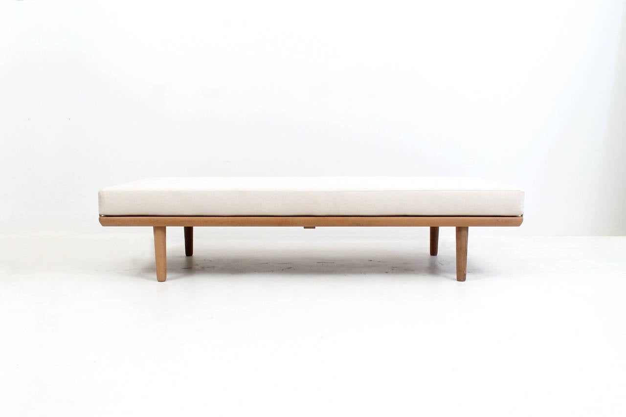 Tasteful daybed or bench by Danish designer Hans Wegner for Getama. Solid oak frame with brass supports that hold cushion in place. Recently reupholstered in linen with leather button detailing.