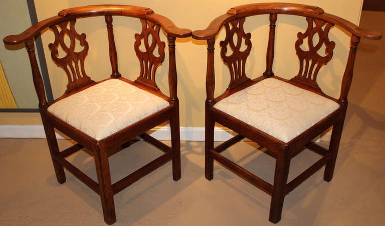 This wonderful pair of fruitwood corner chairs, probably English,  feature nicely carved scrollwork backs, turned arm supports, and sturdy leg and stretcher construction. Reupholstered slipseats.