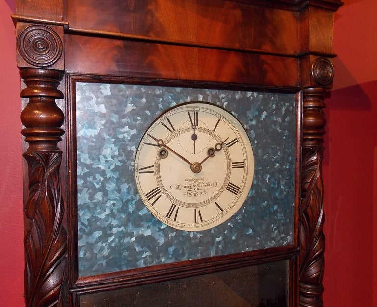 A circa 1831 to 1833 Munger & Benedict mahogany shelf clock, Auburn, New York. Having turned and acanthus carved half columns flanking the full-length door with looking glass and blue tin dial surround, painted iron dial signed Warranted by Munger &