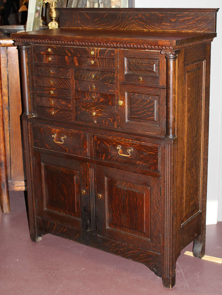 This great dental cabinet in oak was made by American Cabinet Company of Two Rivers, Wisconsin, featuring many custom tool drawers, upper section scroll top columns, original hardware and a paneled back.