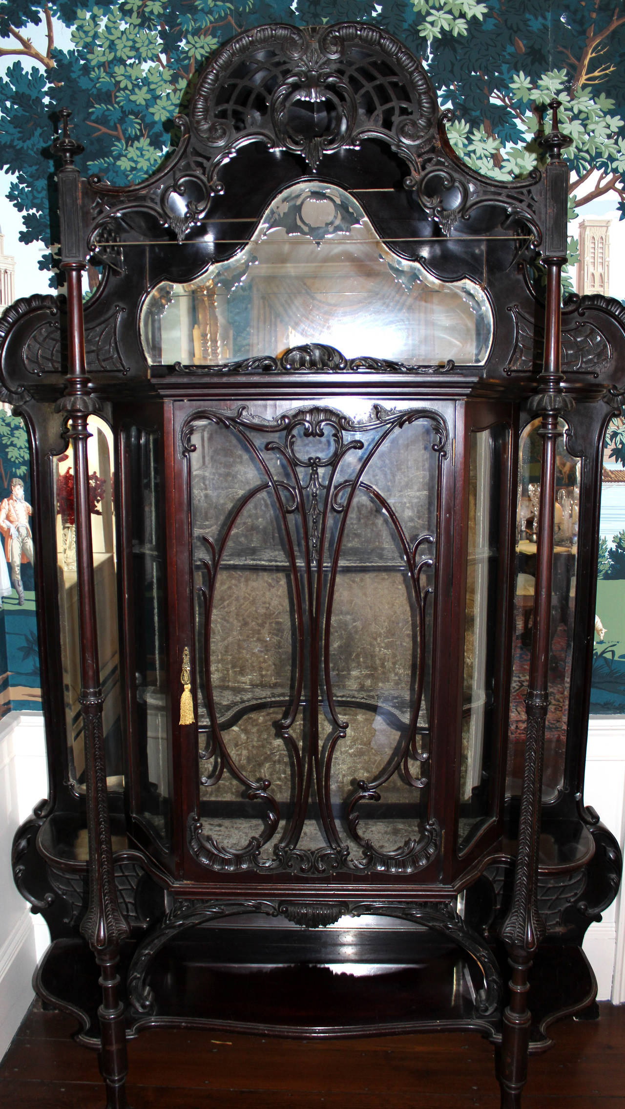 Chinese Chippendale display cabinet in mahogany. The pierced and arched rocaille, foliate carved and scrolling bonnet surmounts a cabinet with glazed door flanked with beveled mirrors and turned pillars terminating in ball and claw feet. Velvet