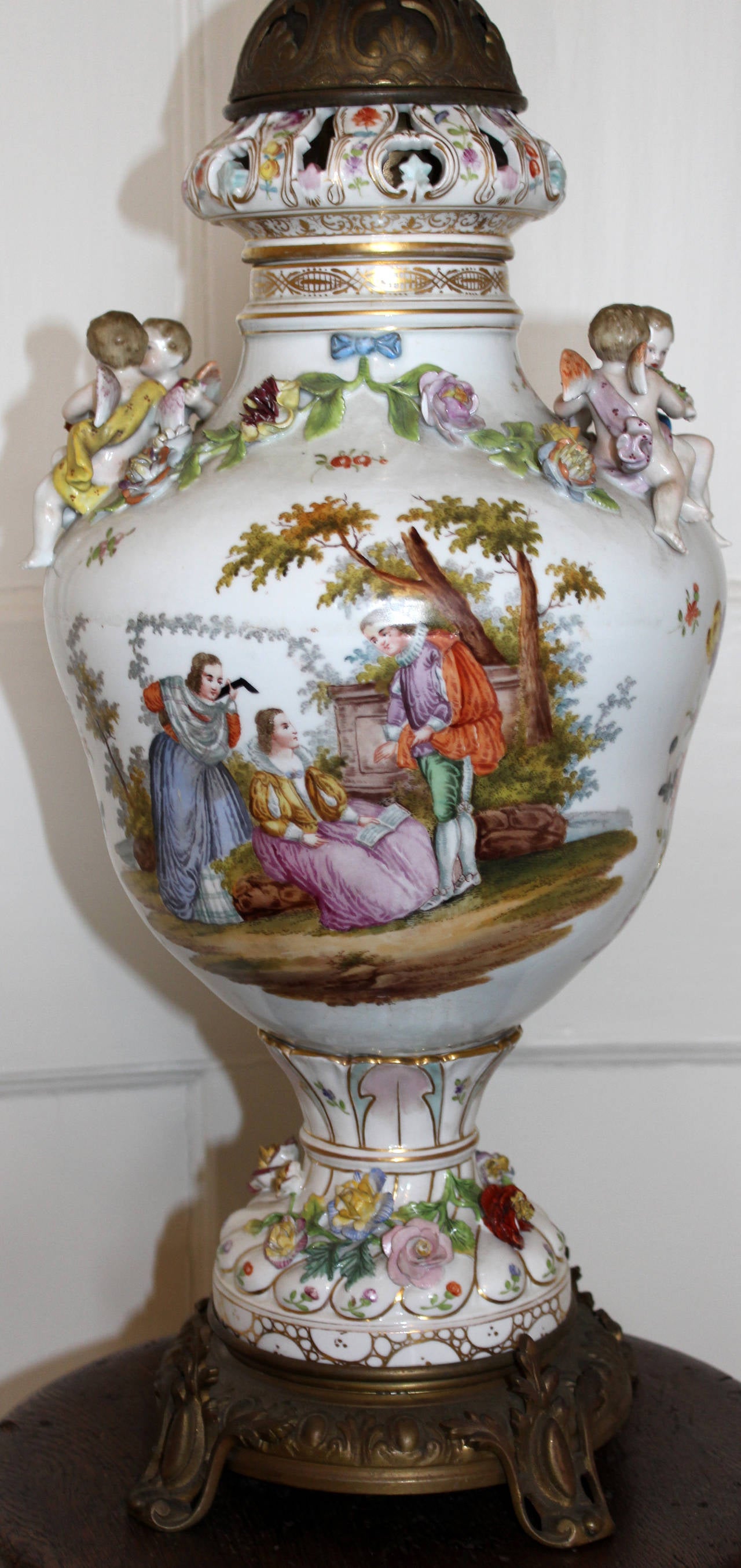 Meissen table lamp with applied cherubs, floral swags and decorations. Hand painted decoration depicts figures in a classical setting reading and playing music. Decorative brass footed base and fixture.