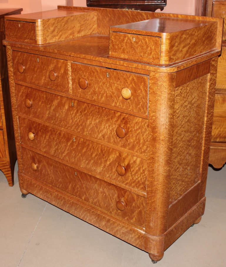 19th century chest of drawers of bird's eye maple. The top with two glove drawers above a case of two short over three long drawers with wooden turned knobs and raised on ball feet with casters.