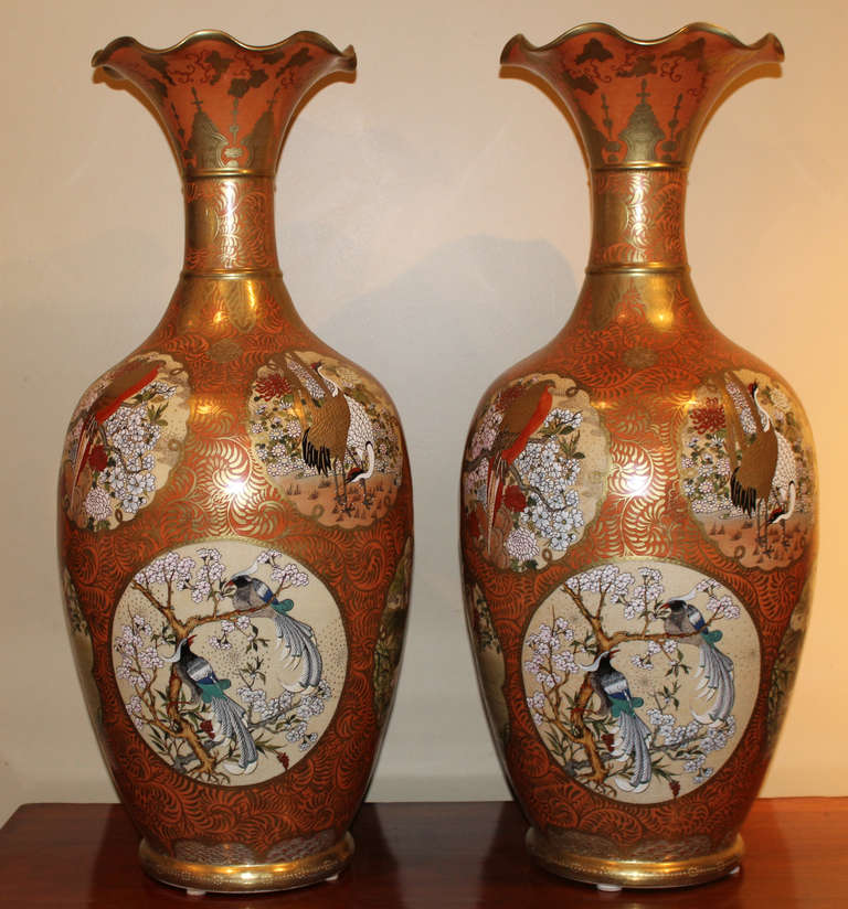 Spectacular pair of large Japanese Kutani style porcelain vases with everted, fluted rims and banded necks rising from elongated ovoid bodies. The color is predominately orange and gold gilt, depicting birds and floral scenes. Each is signed on the