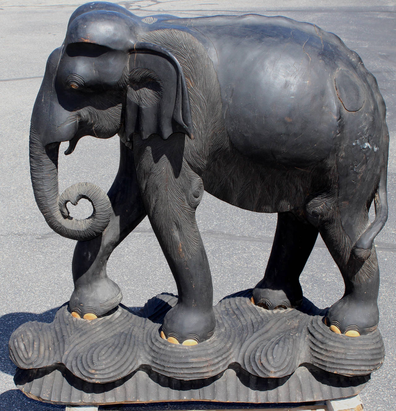 A large hardwood ebonized hand carved elephant, probably from India with inward curled trunk and nice detail. Some finish restorations and toe losses, as well as shrinkage cracks.  A circular patch added on its back, perhaps to replace a tree knot