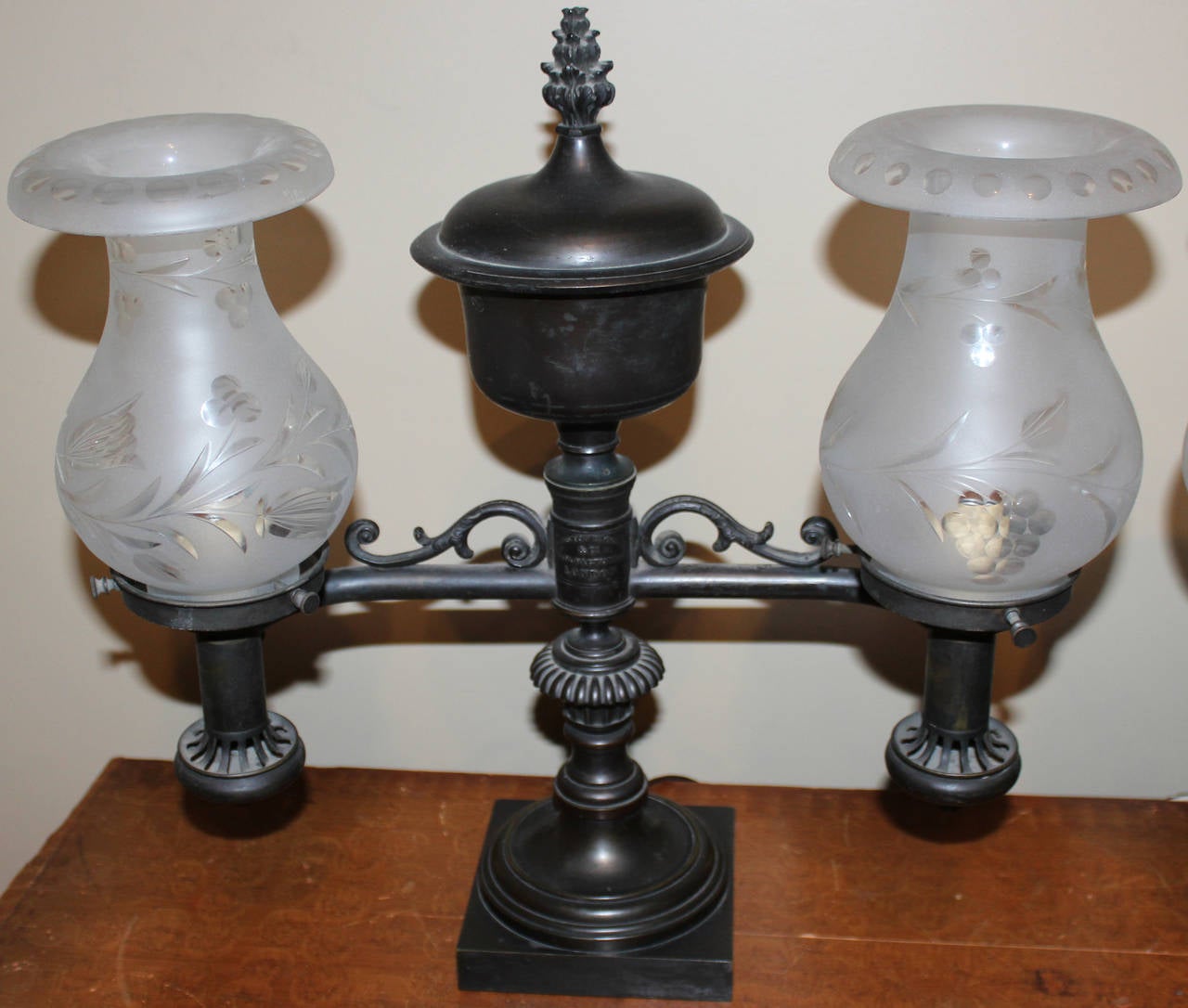 Pair of bronze double burner Argand lamps, English, mid-19th century,
Central pedestal with urn form pediment and square base. Two flanking arms support burners with wheel etched glass frosted shades. Each lamp shows a label “Johnston Brookes & Co.