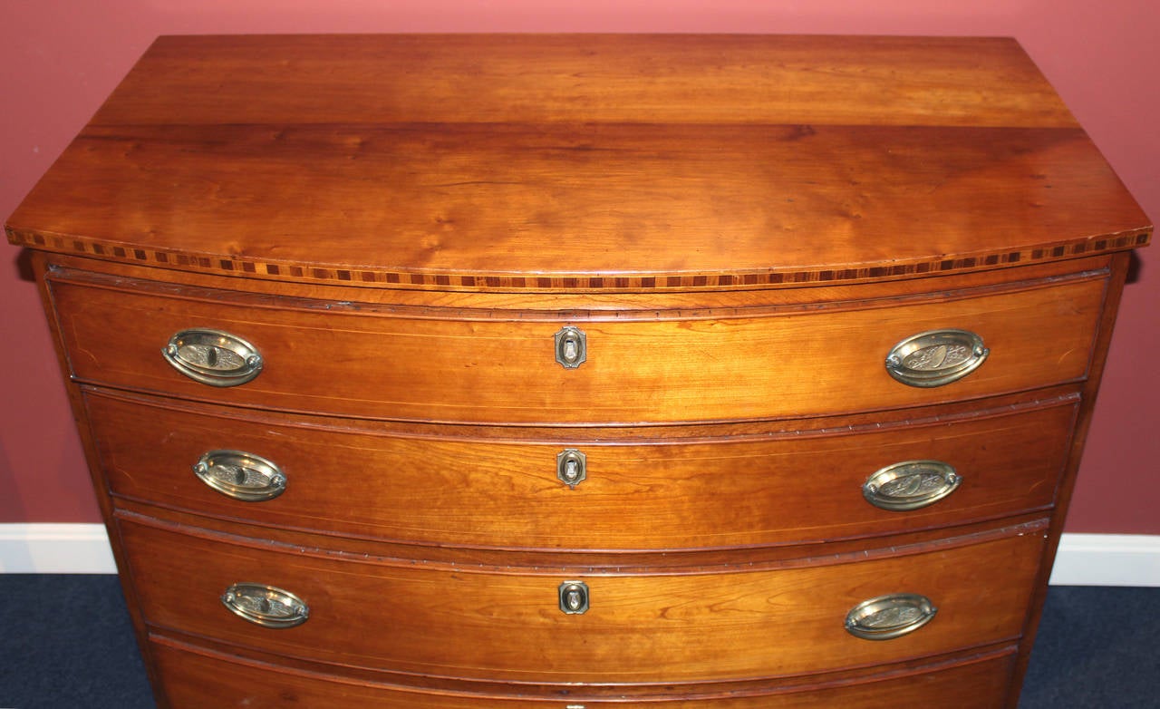 A fine Federal Period cherry four drawer bow front chest, New England circa 1800,  the top with banded edges over a conforming case with four string-inlaid, cockbeaded, graduated drawers, on French feet. Original brasses, signed HJ. According to