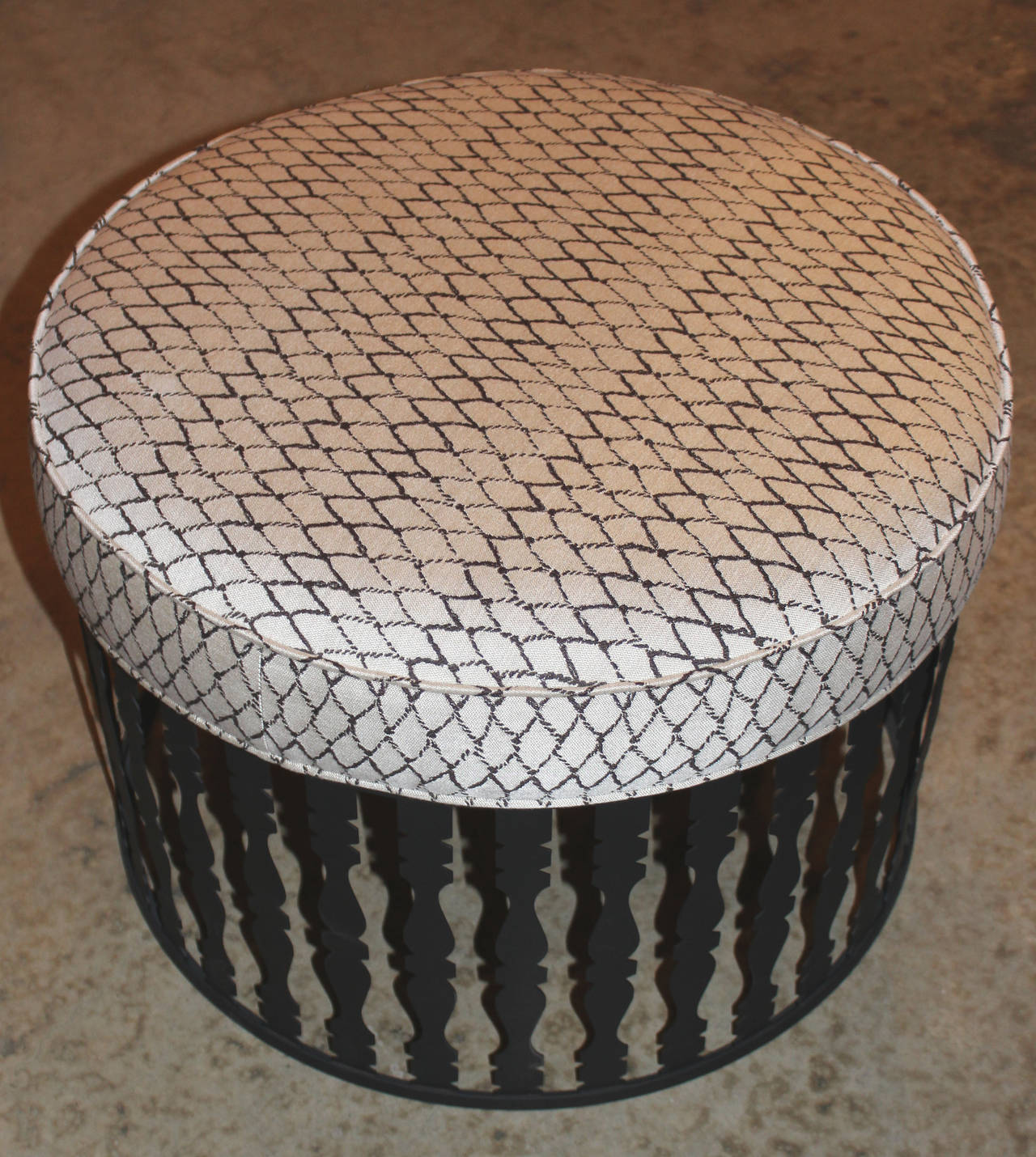 A pair of round metal ottomans designed by Arthur Umanoff probably for Shaver Howard, Mid-Century, with a flat black base finish with cushioned seats appointed with geometric upholstery.