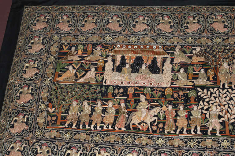 This large Burmese wall tapestry shows Intricate needlework incorporating beads, glass stones, sequins, silver and gold threads and appliqués using a variety of textiles on a black background. Detailed central scene showing various figures 
